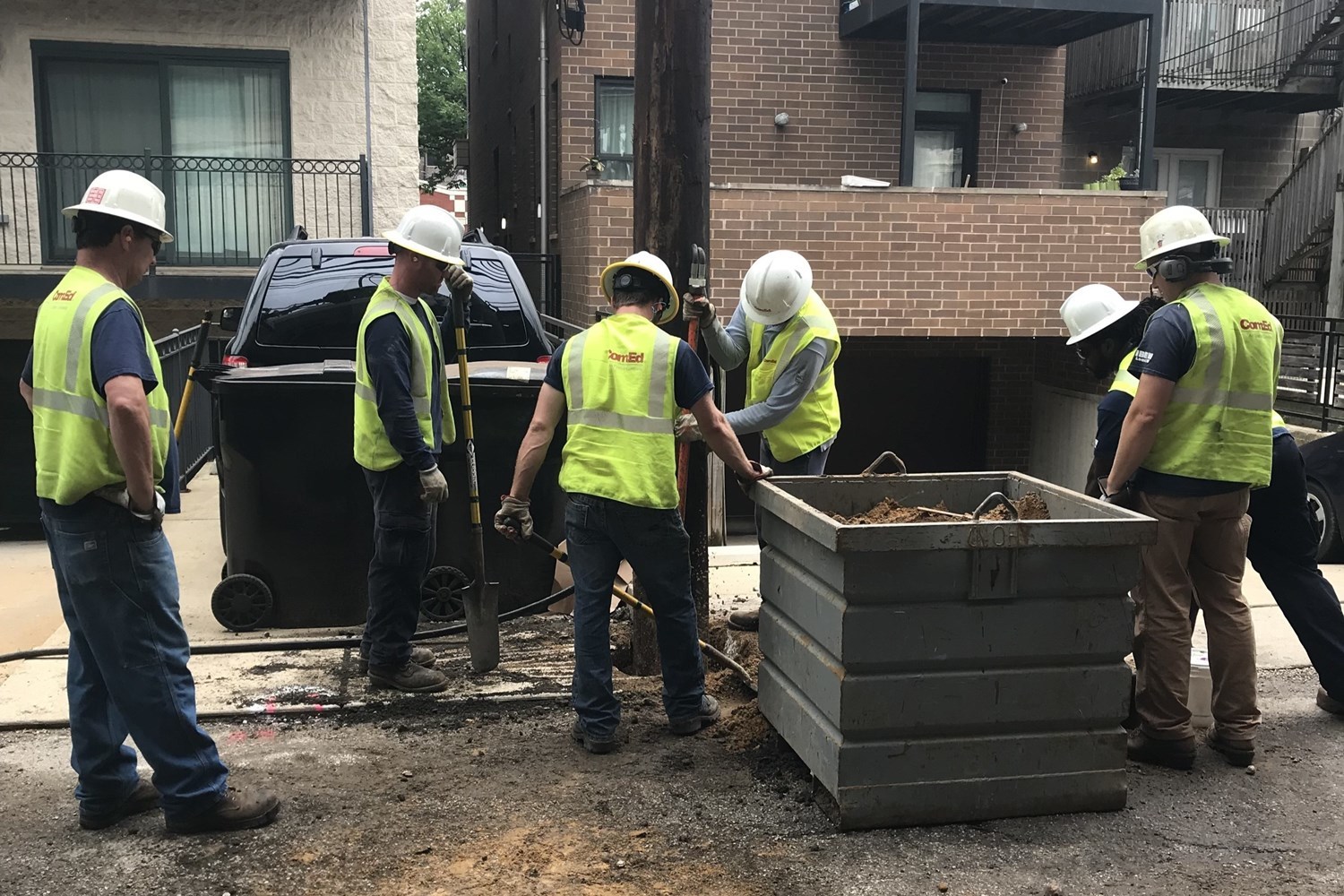 A construction crew in yellow work vests performing utility work around the base of an electrical pole.