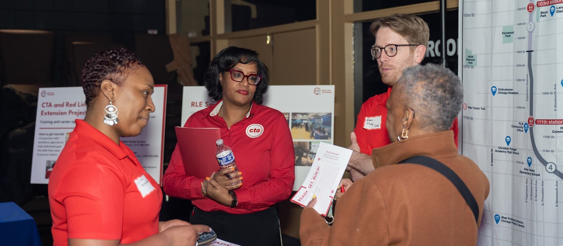 Four people having a conversation at a community meeting in front of poster boards explaining the RLE project.