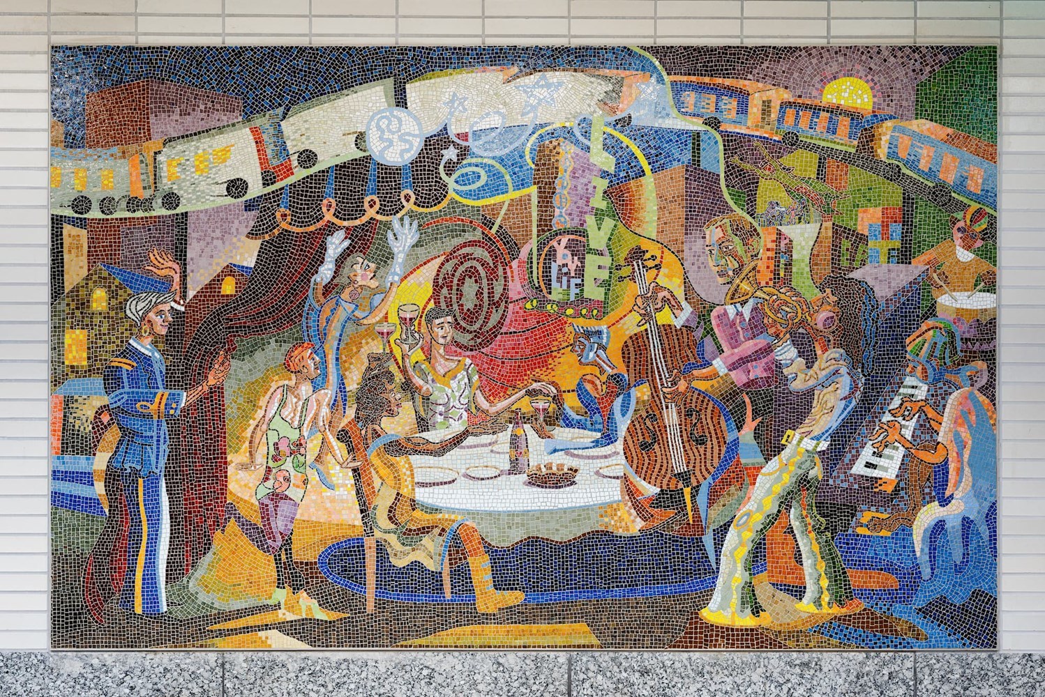 Colorful mosaic on station house wall. Red and gray spinning oval, musicians, neighbors gathering around a communal table.