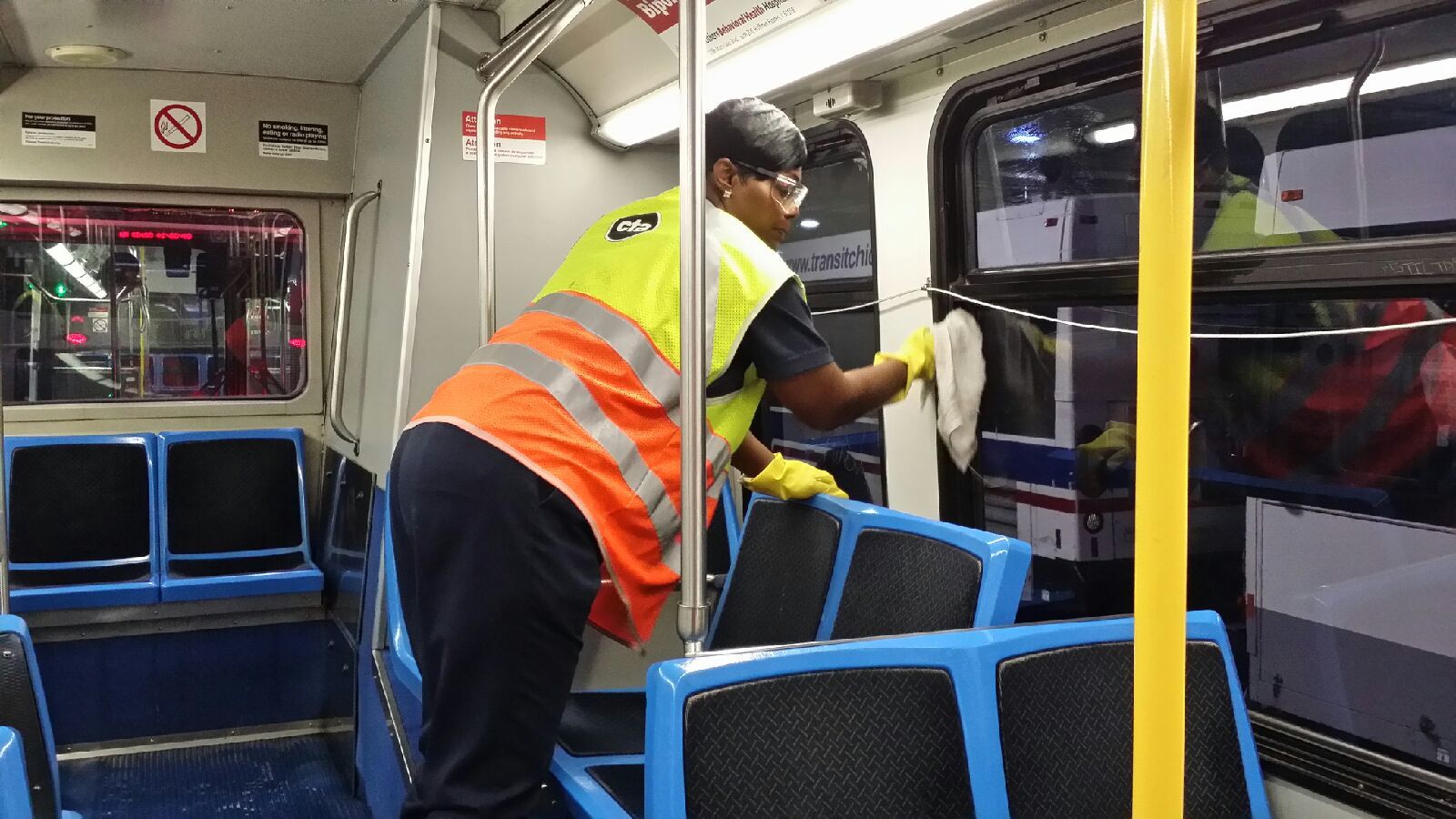 Female CTA worker shown cleaning interior of bus.